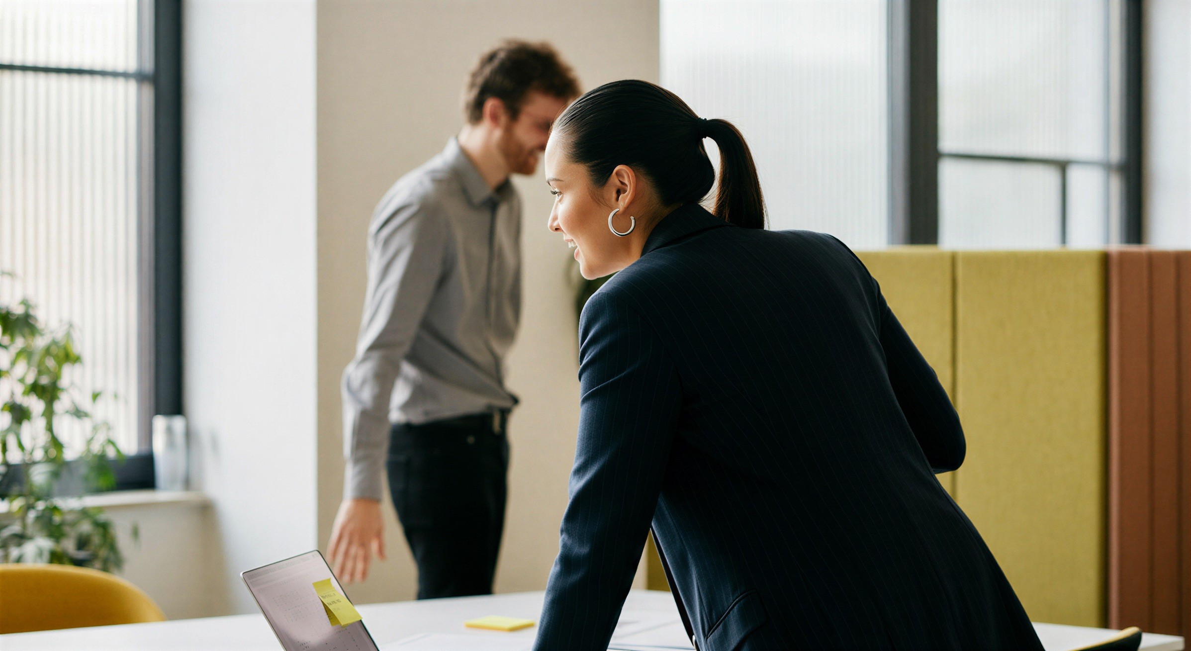 Une femme penchée sur un bureau, un collègue debout derrière elle, dans un bureau lumineux.